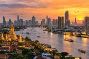 Bangkok skyline and Chao Phraya River at sunset with temple spires and a distant aircraft